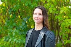 Kvinna i svart jacka står framför en grönskande bakgrund.