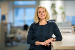 Kvinna i kontorsmiljö, leende och klädd i en mörkblå tröja.