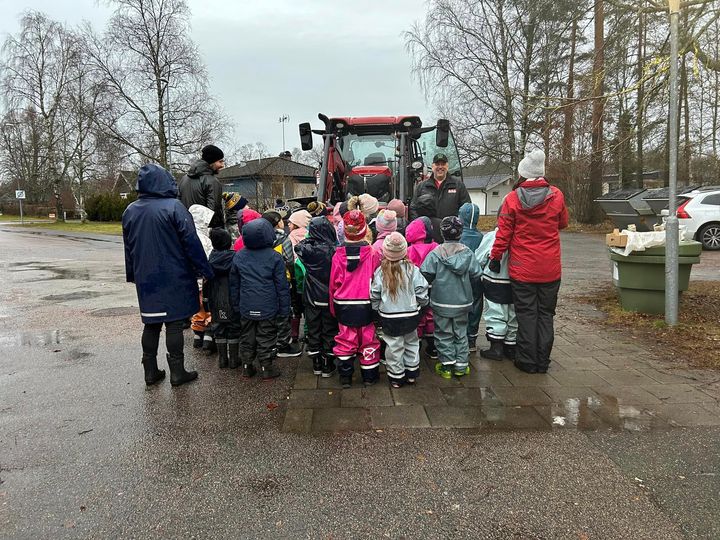 Barn i regnkläder har samlats runt en traktor.