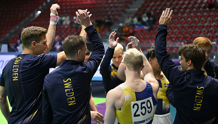 Ett svenskt gymnastiklag står i en cirkel och hejar på varandra.