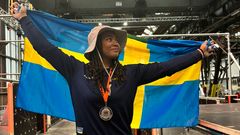 Person med silvermedalj håller upp en svensk flagga bakom sig och ler.