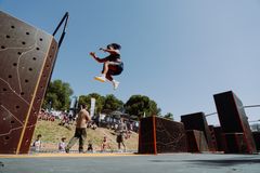 Kvinna i luften under parkourtävling, människor i bakgrunden.