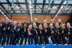 En grupp glada gymnaster firar tillsammans på en prispall med sina medaljer.
