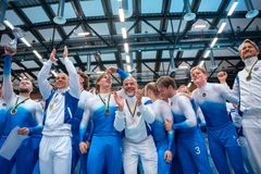 Grupp av glada personer firar med medaljer och pokal inomhus.