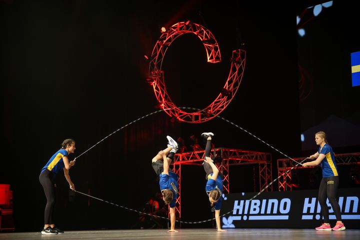 Fyra personer hoppar hopprep under en tävling, iklädda blå och gula sportkläder.