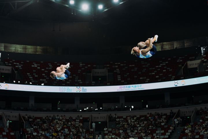 Två gymnaster utför volt i luften under en tävling i en arena.