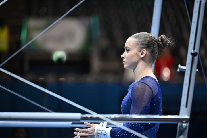 En kvinnlig gymnast i en blå dräkt står vid en gymnastikbar.