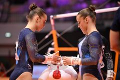 Två gymnaster förbereder sig vid barren, klädda i mörka dräkter.