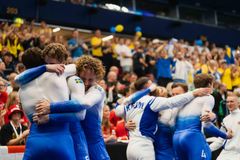 Gymnaster i blåvita dräkter kramar varandra. Bakom dem finns en jublande publik med svenska flaggor.