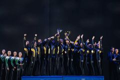 Ett gymnastiklag i svarta dräkter står på prispallen med uppsträckta armar och håller pokaler.