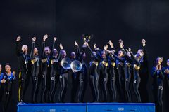 Grupp av kvinnor i gymnastikdräkter firar på en prispall med pokaler.