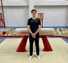 En man i träningskläder står leende framför en gymnastikbygel i en träningslokal.