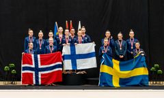 Gymnaster från Sverige, Norge och Finland poserar med medaljer och flaggor på en prispall.