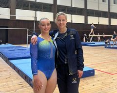 Två personer står tillsammans i en gymnastiksal. Den ena har en blå gymnastikdräkt, och den andra har en sportig jacka.
