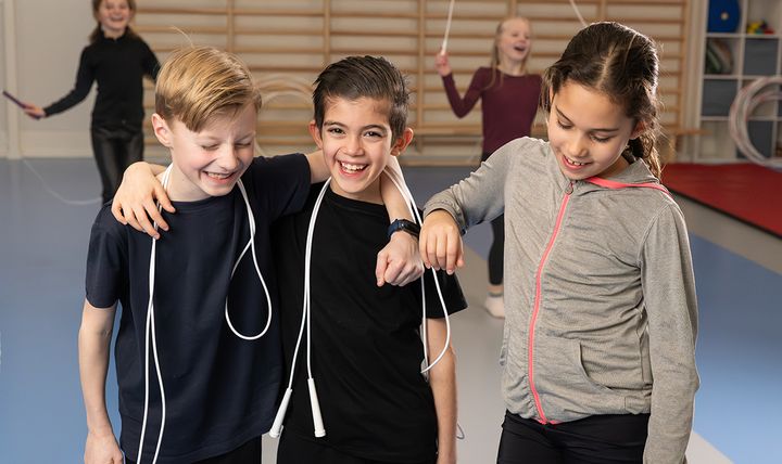 Tre barn i en gymnastiksal som skrattar och håller i hopprep.