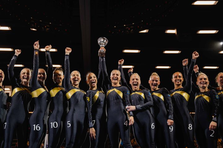 Ett gymnasteam jublar och håller upp en pokal efter att ha vunnit SM-guld i damklassen.