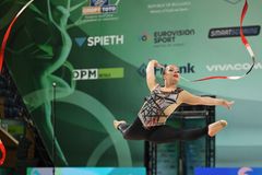 Gymnast utför ett hopp med ett band i luften under en tävling.