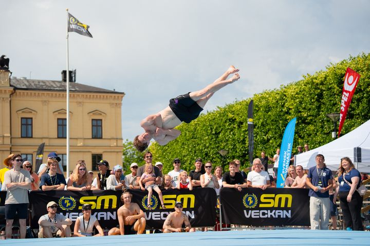 En man utför avancerade gymnastiska trick i luften inför en publik under SM-veckan.
