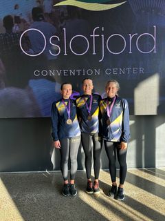 Tre personer i sportkläder med medaljer runt halsen står framför en skylt vid Oslfjord Convention Center.