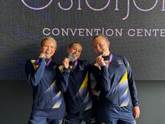 Tre personer i träningskläder poserar med medaljer vid ett evenemang.