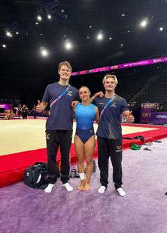 William Sundell, Emelie Westlund och David Rumbutis står på tävlingsgolvet i en gymnastikarena i Paris.