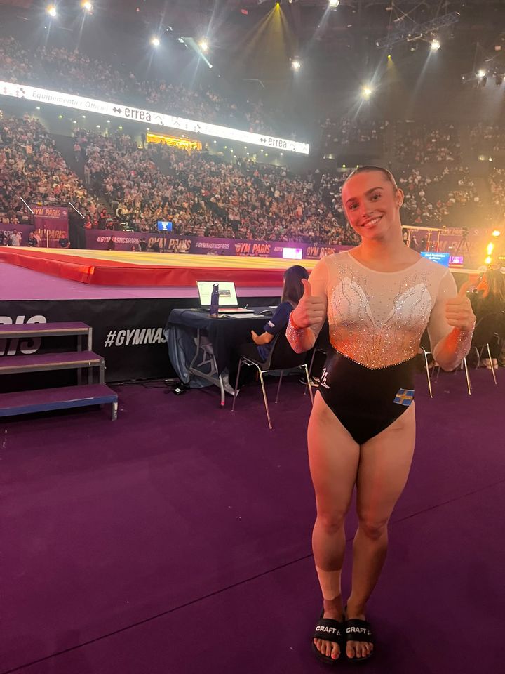 Emelie Westlund ler och visar tummen upp i tävlingsarenan efter att ha kvalificerat sig till dubbla finaler.
