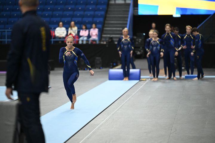 Gymnast springer mot redskapet medan laget väntar bakom.