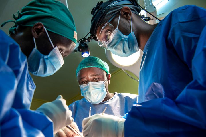Tre läkare i operationskläder står lutade över en patient under operation.