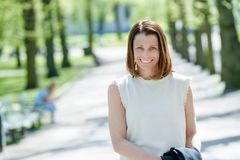 Kvinna i vit topp står i park och ler in i kameran.