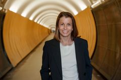 Kvinna i vit topp och svart kavaj ler in i kameran, gul lite suggestiv tunnel i bakgrund.