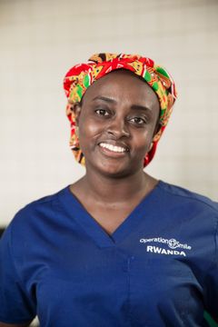 Kvinna med blå läkarkläder och färgglad scrubmössa ler mot kameran. Halvporträtt.