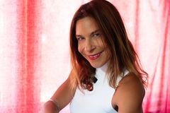 Kvinna med axellångt brunt hår och en vit topp ler mot kameran. Halvfigur, röd bakgrund.