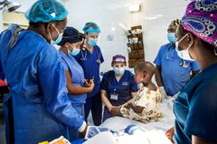 Sjukvårdsklätt team står runt om ett barn som sitter på en säng i en sjuksal.