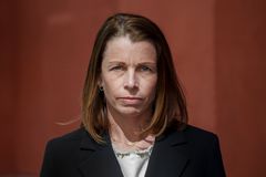 Kvinna i vit topp och svart kavaj tittar, med allvarlig min, in i kameran, vinröd bakgrund.