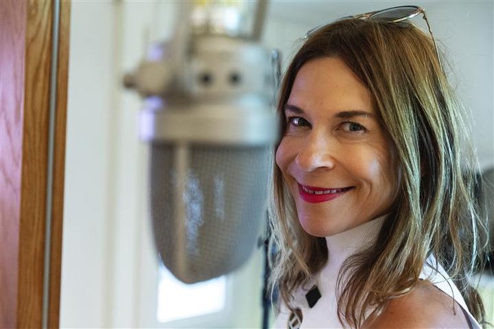 Kvinna med brunt axellångt år och vit topp står bakom mikrofon. Hon är i fokus, micken ur fokus.