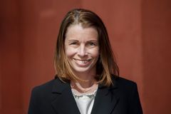 Kvinna i vit topp och svart kavaj ler in i kameran, vinröd bakgrund.