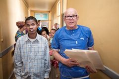En ung man med läppspalt går i en sjukhuskorridor bredvid en äldre man i scrubs, som håller i journaler/papper.