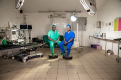 Två mörkhyade, rwandiska, läkarklädda män sitter i en operationssal.