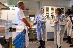 Tre personer iklädda en tunn överdragsklädsel står i sjukhusmiljö och diskuterar/gestikulerar.
