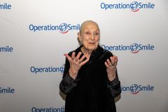 Äldre kvinna ler och gestikulerar mot kameran. I bakgrunden en fotovägg med logotypen "Operation Smile".