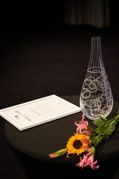 En glasvas samt blommor och diplom på ett bord.