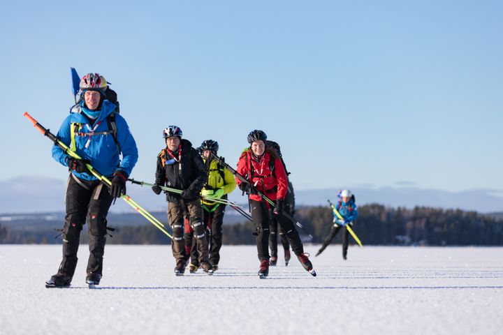 Personer som åker skridsko på naturis med ryggsäck och hjälm.