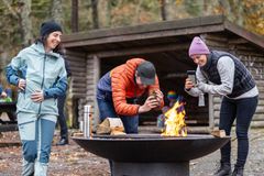 Tre personen runt en eldstad där det brinner en eld.