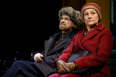 två personer klädda i varma kläder som sitter intill varandra på en bänk.