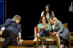 Fyra personer sitter och tittar på en mobiltelefon i en teaterscen.