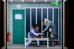 Två personer i ett omklädningsrum, en hjälper den andra att få på sig en stövel.