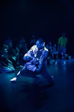 Bild av dansare som uppträder i en dramatisk scen på scenen med publik runtomkring.