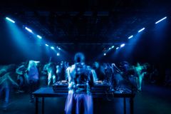 Bild på en DJ som spelar för en dansande publik i ett rum med blå belysning.