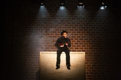 Bild av en person som sitter på en låda och spelar ukulele under strålkastare.