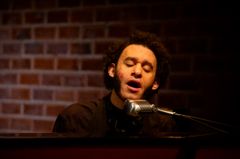 Alt text: En person sjunger i en mikrofon framför en tegelvägg.